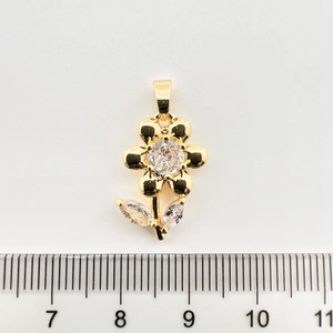 Vue détaillée d'un pendentif fleur plaqué or avec zircon à côté d'une règle métrique