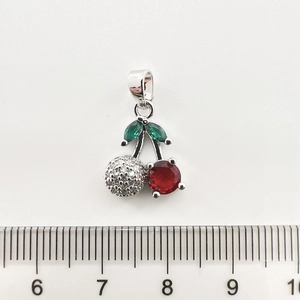 Détail d'un pendentif cerise avec rubis rouges et feuilles vertes à côté d'une règle