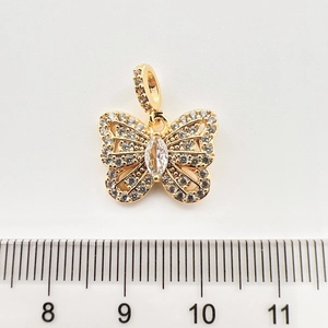 Détail d'un pendentif papillon doré avec zircons à côté d'une règle pour la taille réelle
