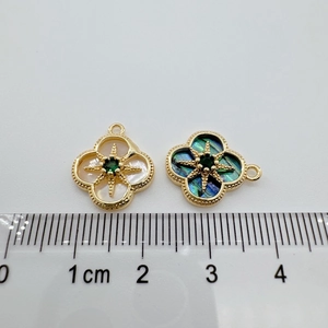 Detalle de dijes de trébol bañados en oro 18K con concha de abulón y gema verde incrustada