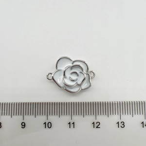 Détail macro d'une breloque camélia en émail blanc de 1,8cm avec bordure argentée et anses