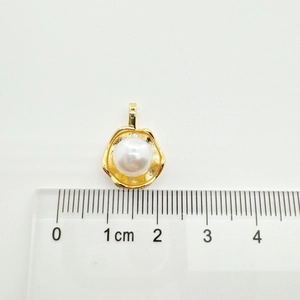 Macro view of a 10mm white pearl pendant with a wavy gold base next to a measuring ruler