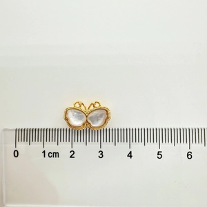 Macro-opname van een gouden vlinderhanger van 1,5 cm met witte schelp inleg naast een liniaal