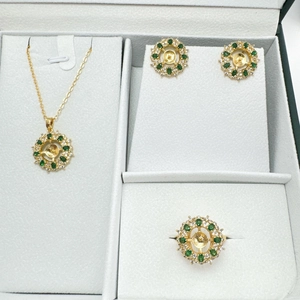 Set di gioielli a fiore dorato con gemme verdi e bianche su velluto grigio