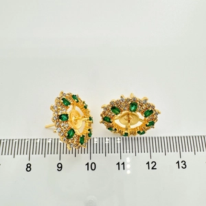 Dettaglio orecchino a fiore dorato con gemma verde e righello che mostra la misura