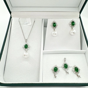 Elegant jewelry set with emerald zircon and pearl accents on a velvet lining