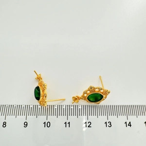 Detailed view of vintage gold stud earrings with green zircon and pearl accents on a ruler