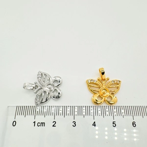 Detailed view of butterfly charms with zircon accents and pearl settings next to a ruler