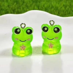 Detailed view of glowing green resin frog charms with pink cherry blossom and silver rings