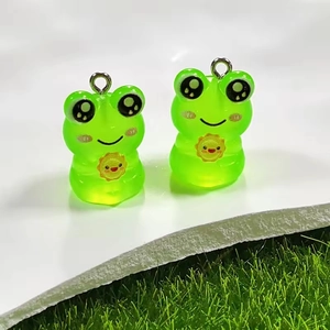 Close-up of cute glow-in-the-dark resin frog pendants with metal rings for DIY jewelry