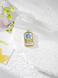 Détail macro du pendentif rectangulaire doré avec fleurs séchées bleues en résine
