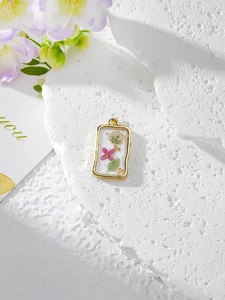 Close-up of golden rectangular resin pendant with pink dried flowers on stone background