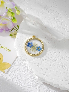 Gros plan du pendentif rond en résine avec fleurs séchées bleues et cadre doré gaufré