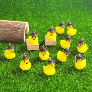 Close-up of twelve tiny yellow resin duck charms with brown hats on green grass