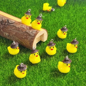 Macro detail of resin yellow duck charms with hats on a green lawn for DIY jewelry making