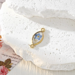 Detail eines Marquise-Harzanhängers mit blauen Trockenblumen und goldenem Metallrahmen