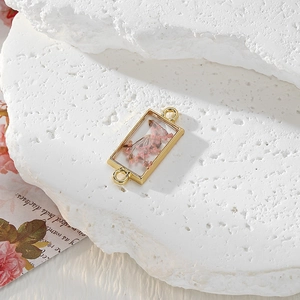 Macro shot of gold geometric pendant featuring pink dried flowers in resin with dual rings