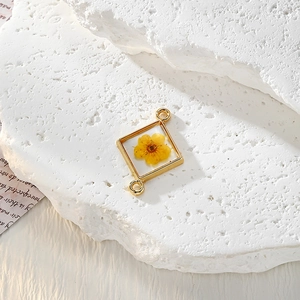 Dettaglio del ciondolo geometrico dorato con un vero fiore giallo essiccato in resina