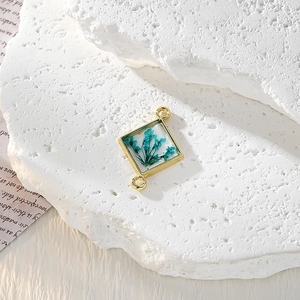 Dettaglio del ciondolo quadrato in resina con veri fiori secchi blu e doppi anelli d'oro