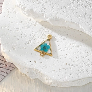 Dettaglio macro del ciondolo triangolare dorato con fiore secco blu in resina
