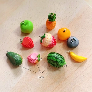 Colorful resin fruit pendant set with metal loops on light wood grain background