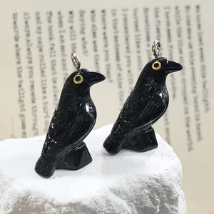 Detailed view of resin black raven charms with yellow eyes on natural stone background