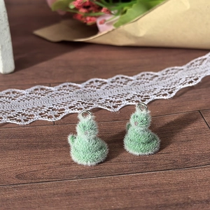 Close-up of cute light green flocked animal charms with silver rings on wood background