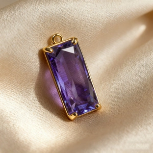 Macro shot of rectangular purple crystal pendant with gold plating on champagne silk fabric
