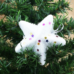 White foam star Christmas ornament with colorful sequins on a green tree branch