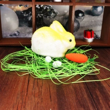 Detail of gradient yellow foam Easter bunny with faux grass and carrot on wood surface