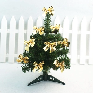 Mini artificial Christmas tree with golden bows and black tripod base on desktop