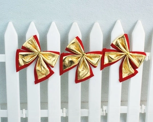 Three red and gold glitter bows hung on a white picket fence for Christmas decoration