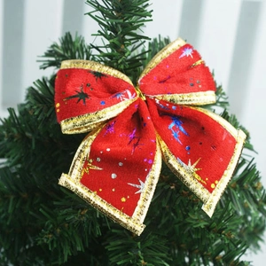 Detail of a red knitted Christmas bow with gold tinsel edges on a green pine tree