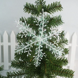 White iridescent Christmas snowflake ornaments hanging on a green Xmas tree branch
