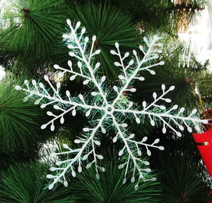 White Christmas snowflake ornament with iridescent tinsel on green pine branches