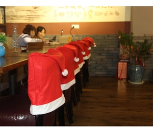 Row of red Christmas hat chair covers with white plush pompoms for dining room decoration