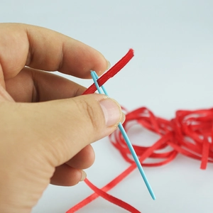 Close-up of threading a red woven ribbon through a light blue plastic needle eye