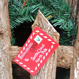 Detail of red felt Santa envelope ornament with gold string on a rustic wood background