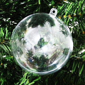 Dettaglio di una pallina di Natale trasparente appesa a rami di alberi verdi