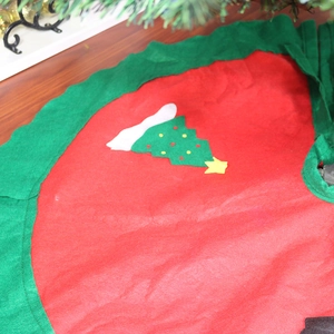 Detail view of 90cm red Christmas tree skirt with green ruffle edge and tree pattern
