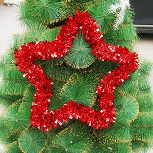 Close-up of fluffy red tinsel star ornament hanging on green Christmas tree branches
