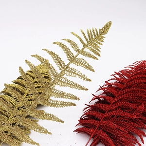 Close-up of sparkling gold and red artificial fern leaves with glitter coating for decor