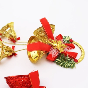Close-up of golden Christmas bell with red bow and pine needle accents on white base