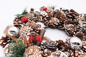 Detailed close-up of Christmas wreath with snowy pinecones, red berries and silver baubles