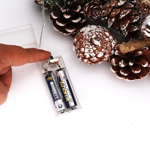 Detail of the transparent LED light battery box on a white pine cone Christmas wreath