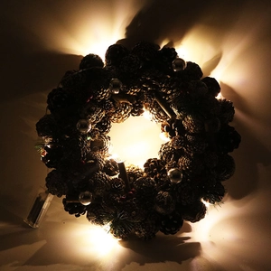 Detail of warm LED lights on a 37cm white pine cone Christmas wreath with silver berries