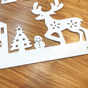 Detail of white laser-cut Christmas reindeer and tree decorations on a wooden surface