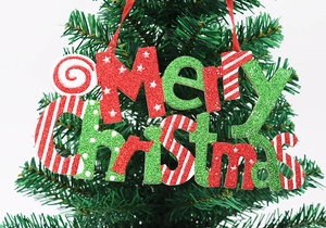 Close-up of Merry Christmas glitter sign hanging on a lush green Christmas tree