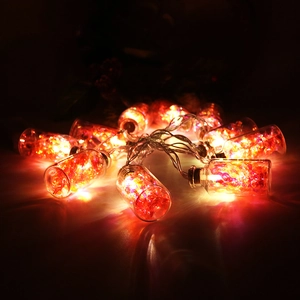 Close-up of LED Christmas light string with glowing red glass bottles on black background