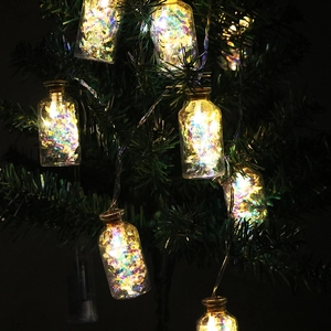 Close-up of glass jar LED fairy lights with colorful iridescent sequins on a pine tree